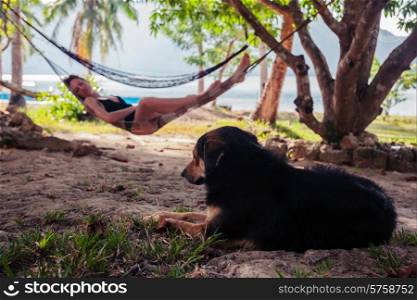 A young woman is relaxing in a hammock with a cute dog in the foregroud