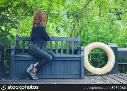 A young woman is relaxing on a bench outside in nature