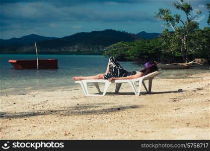 A young woman is relaxing on a sunbed on a tropical beach