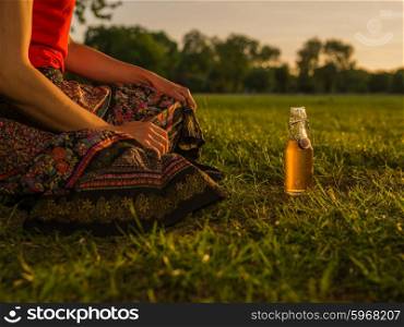 A young woman is relaxing with a beverage in the park at sunset