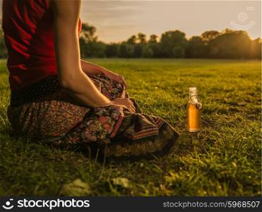 A young woman is relaxing with a beverage in the park at sunset