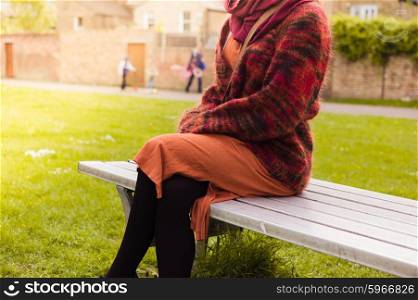 A young woman is resting and relaxing on a bench in the park on a sunny day