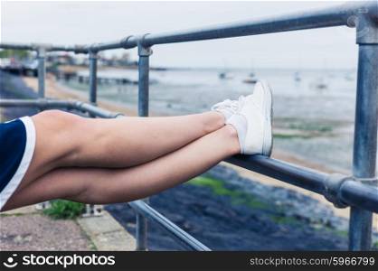 A young woman is resting her feet on a railing by the sea