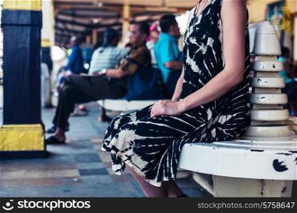 A young woman is seated and is waiting on the platform in a train station