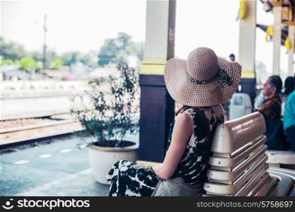 A young woman is seated and is waiting on the platform in a train station