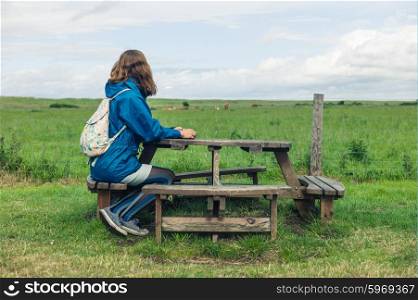 A young woman is sitting a picnic table outside in a field