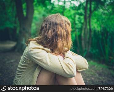 A young woman is sitting alone in the forest