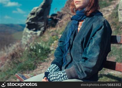 A young woman is sitting and relaxing on a bench in the mountains