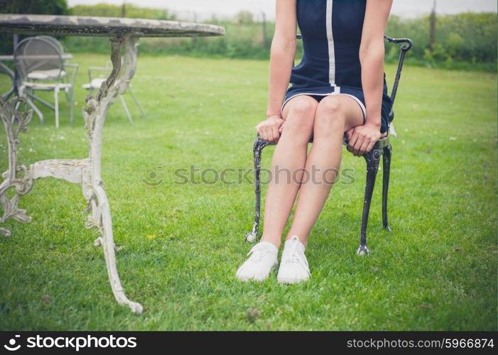 A young woman is sitting and relaxing on a chair on a lawn in a garden
