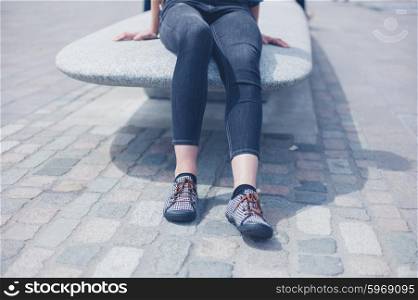 A young woman is sitting and relaxing on a granite bench in the city