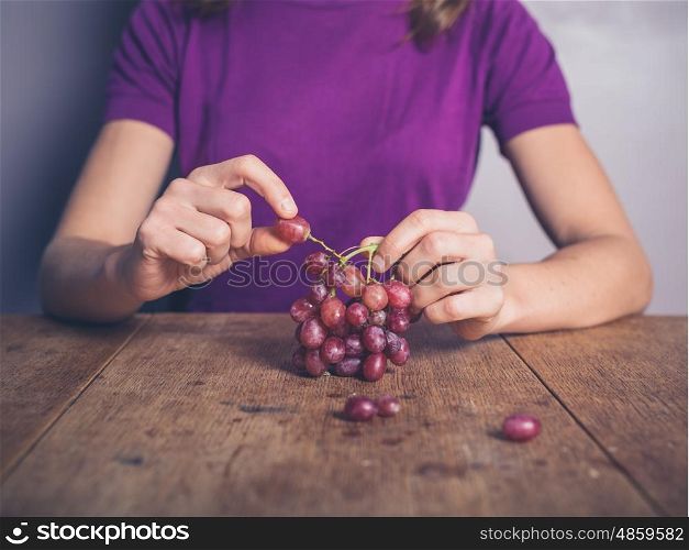 A young woman is sitting at a table and eating grapes