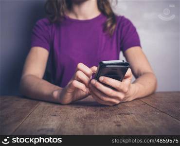 A young woman is sitting at a table and is using a smartphone