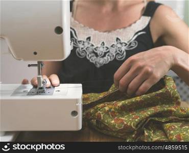 A young woman is sitting at a table at home and is using a sewing machine