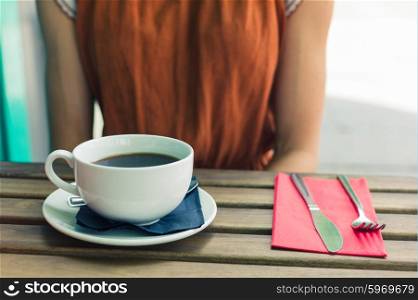 A young woman is sitting at a table outside and is having a big cup of coffee