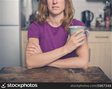 A young woman is sitting at a table with a cup of tea in a kitchen