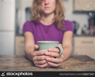 A young woman is sitting at a table with a cup of tea in a kitchen