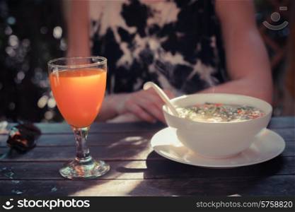A young woman is sitting at a table with a glass of juice and a bowl of soup