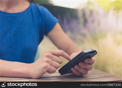 A young woman is sitting at at table outside and is using her smart phone on a summer day