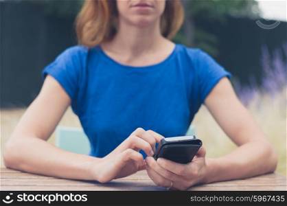 A young woman is sitting at at table outside and is using her smart phone on a summer day