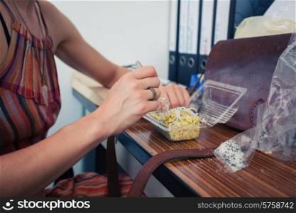 A young woman is sitting at her desk and is having lunch