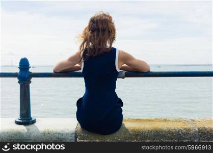 A young woman is sitting by a railing on a promenade by the seaside