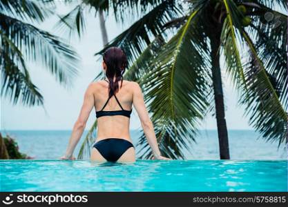 A young woman is sitting by the edge of an infinity pool by the ocean