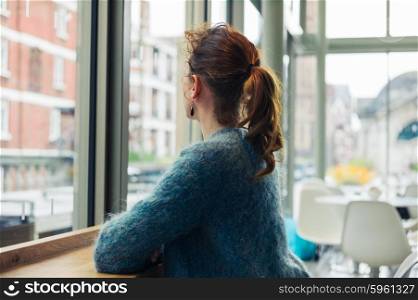A young woman is sitting by the window and is looking out