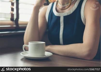 A young woman is sitting by the window in a diner and is having a cup of coffee
