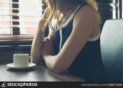 A young woman is sitting by the window in a diner and is having a cup of coffee
