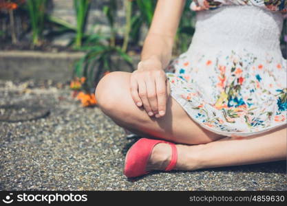 A young woman is sitting in a meditation pose outside on the ground by some flowers