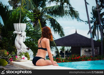 A young woman is sitting in a swimming pool with palm trees and the ocean in the background