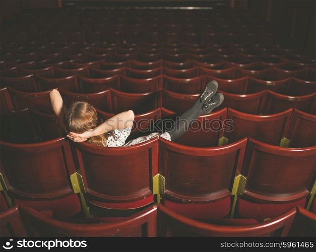 A young woman is sitting in an auditorium with her feet on the seats in front
