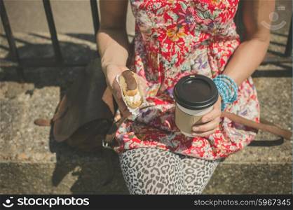 A young woman is sitting in the street with coffee and cake