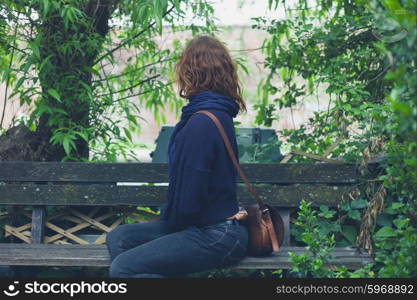 A young woman is sitting on a bench in a forest