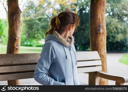 A young woman is sitting on a bench in a shelter in the park