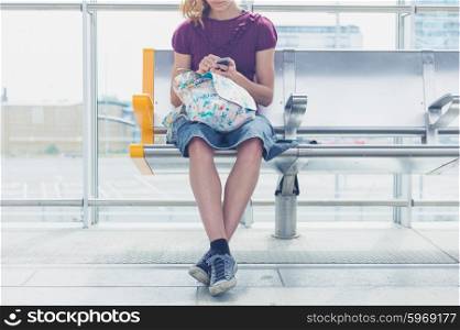 A young woman is sitting on a bench in a terminal and is using her smart phone