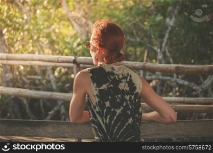 A young woman is sitting on a bench in the jungle at sunset