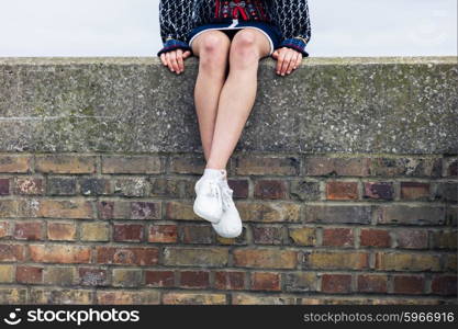 A young woman is sitting on a brick wall and is relaxing