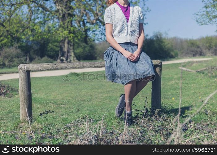 A young woman is sitting on a fence in the forest