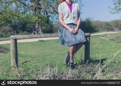 A young woman is sitting on a fence in the forest