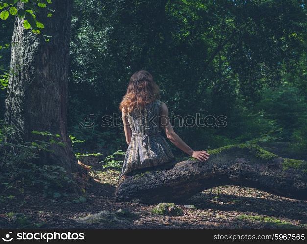 A young woman is sitting on a log in a clearing in the forest