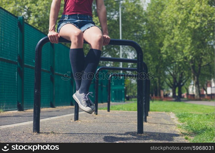 A young woman is sitting on a rail in a park on a summer day