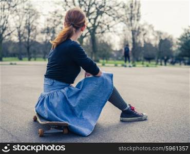 A young woman is sitting on a skateboard in the park