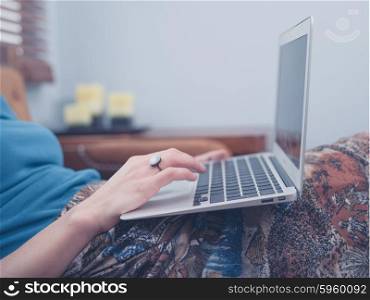 A young woman is sitting on a sofa at home in her living room and is using a laptop computer