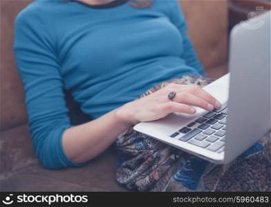 A young woman is sitting on a sofa at home in her living room and is using a laptop computer