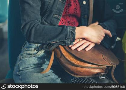 A young woman is sitting on a train and is clutching a handbag