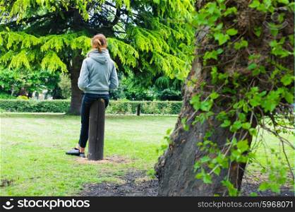 A young woman is sitting on a wooden post in the park