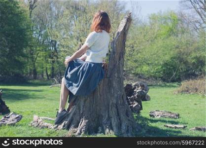 A young woman is sitting on large tree trunk in a forest