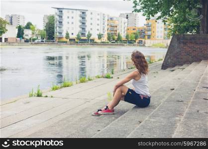 A young woman is sitting on some steps by a marina in the city
