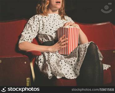 A young woman is sitting on the front row in a movie theater and is watching an exciting film while eating popcorn